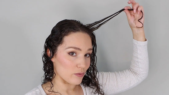 Frau, die ihr dunkelbraunes, gewelltes Haar mit Bouclème-Produkten stylt